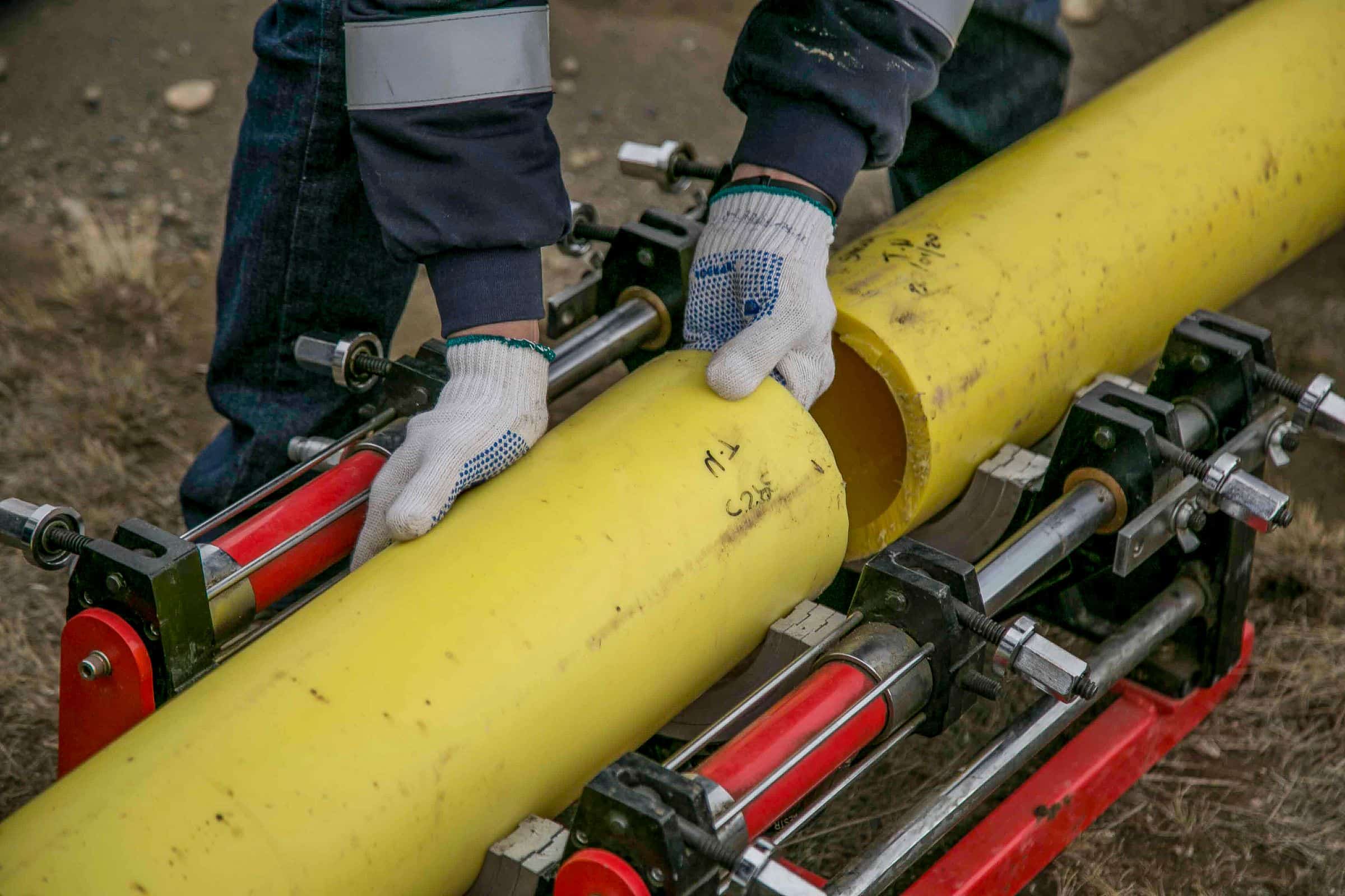 Handen in werkhandschoenen leggen een gele gasleiding in een lasmachine